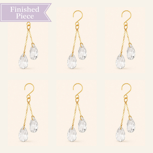 Six clear crystal plant vine suncatcher charms with gold-tone hooks arranged on a warm ivory background.