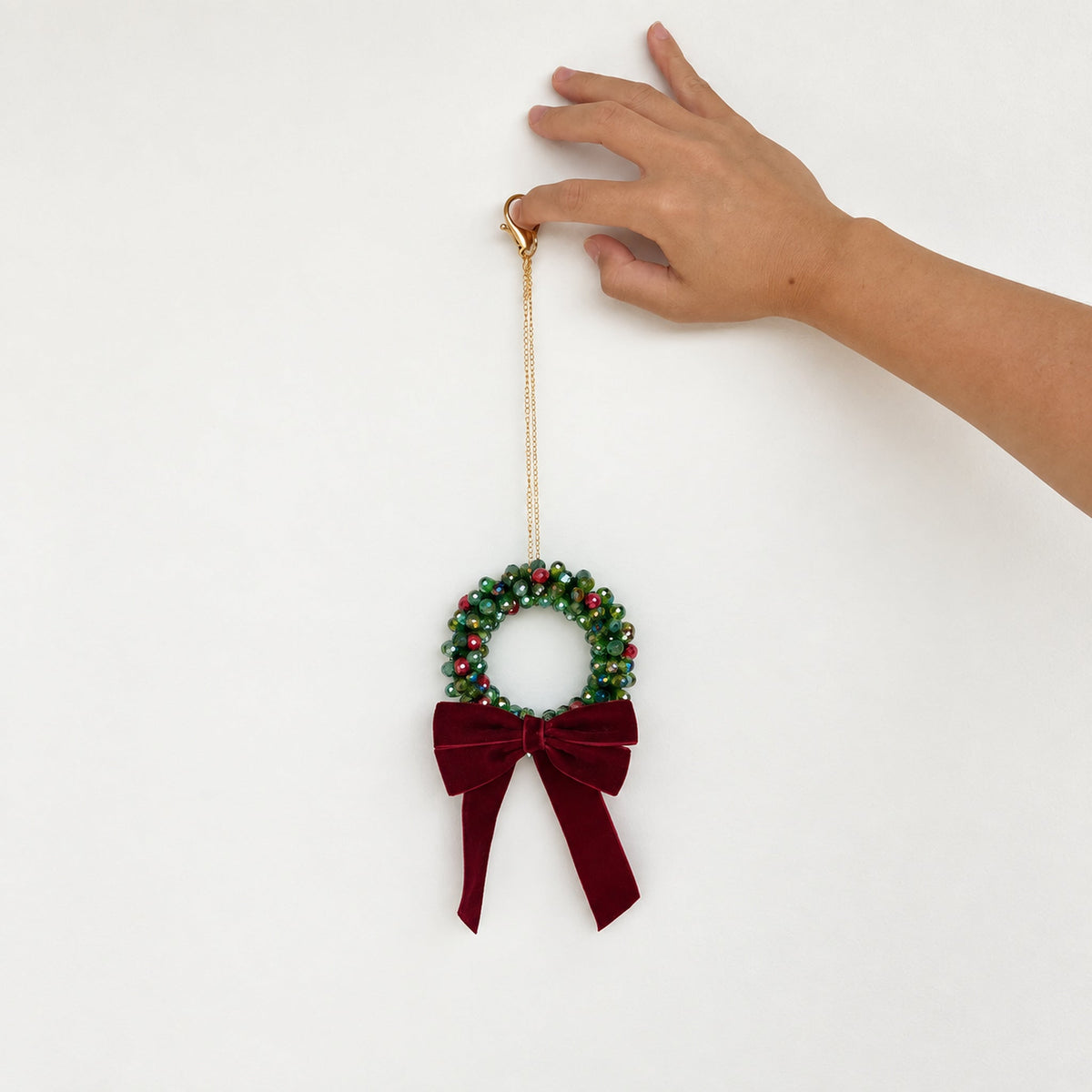Hand holding a Mini 9 cm beaded Christmas wreath by its gold clasp and hanging chain