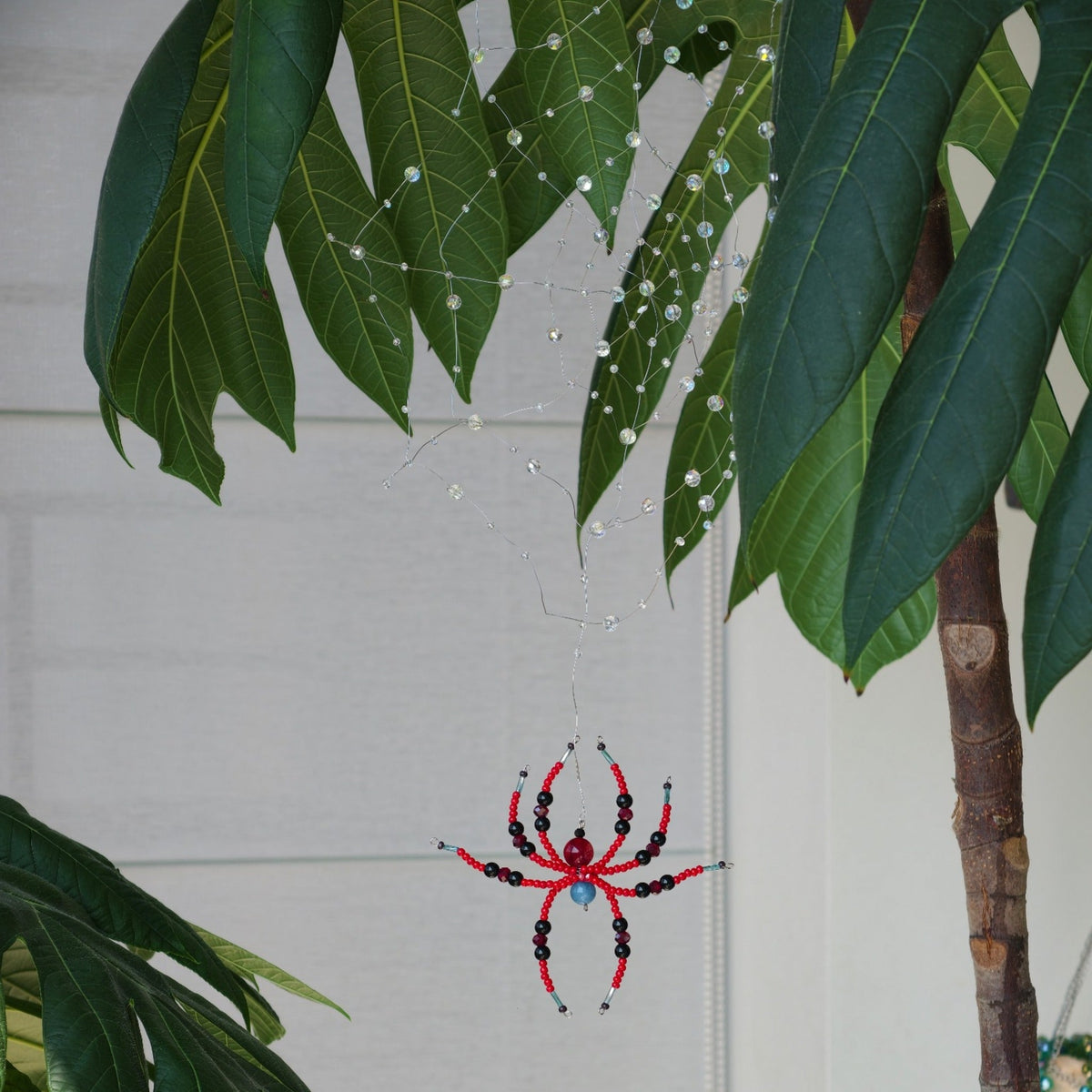 Real photograph of a clear beaded spider web and red and black spider hanging among green leaves