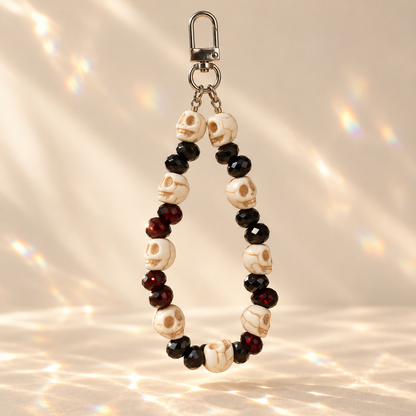 Skull and blood-red beaded phone and bag charm with a swivel clasp on a warm cream background.