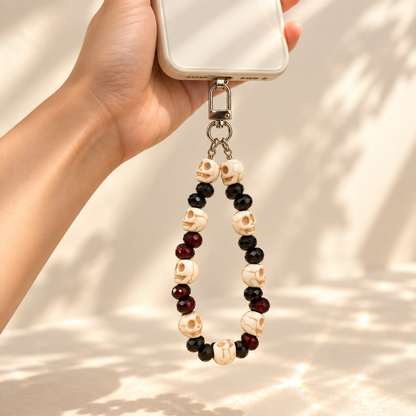 Skull and blood-red beaded charm clipped to a black handbag in a warm Halloween setting.