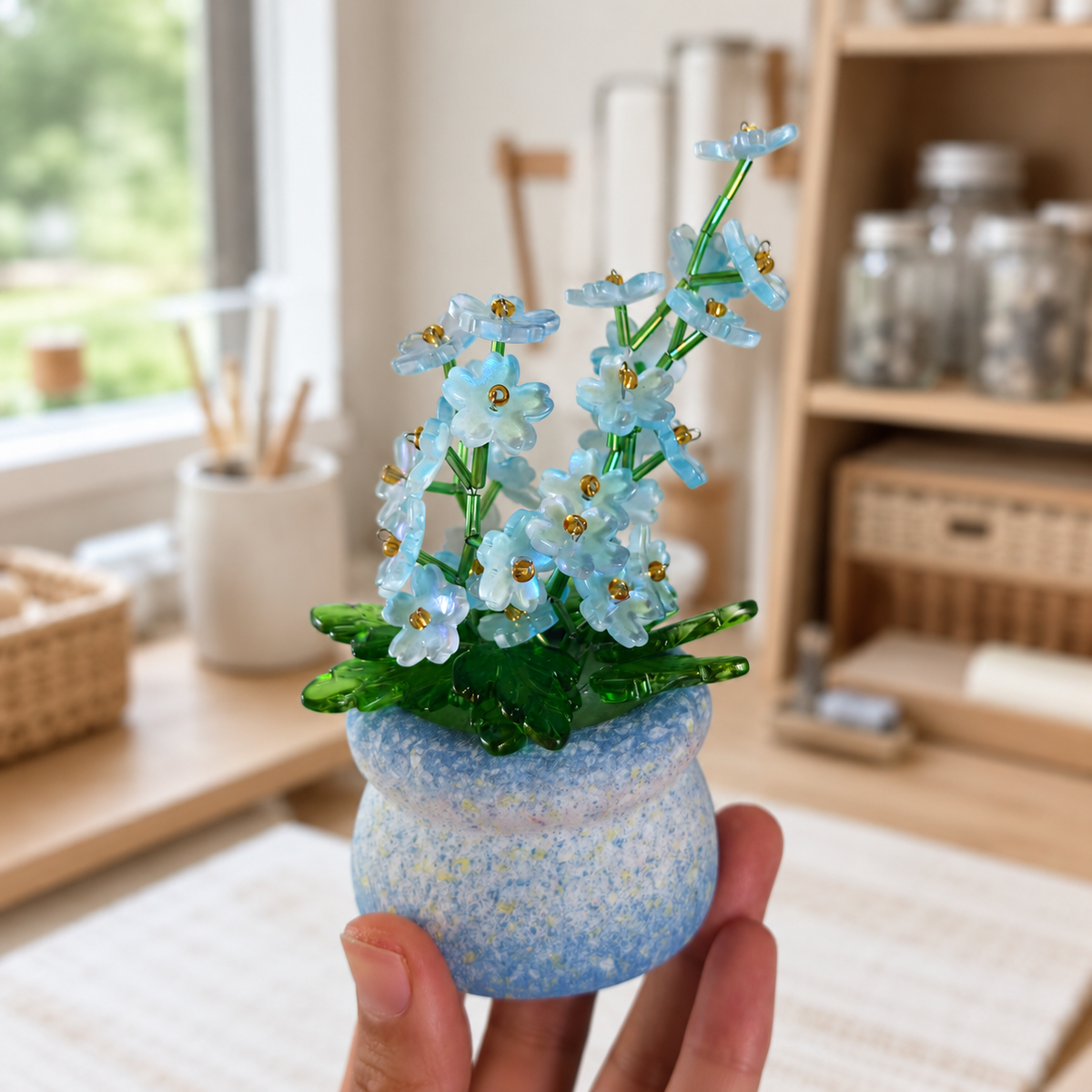 Hand holding a mini blue forget-me-not beaded plant for size reference