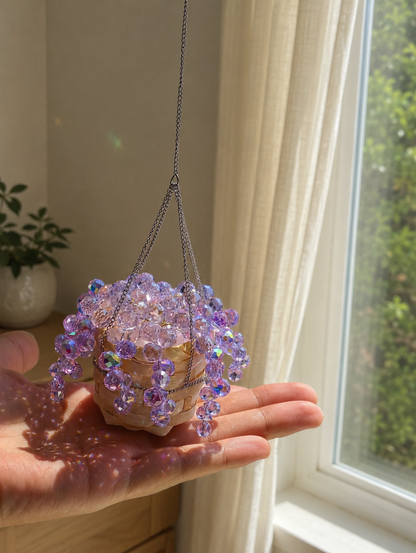 Hand holding a palm-sized finished purple beaded plant beside a window.