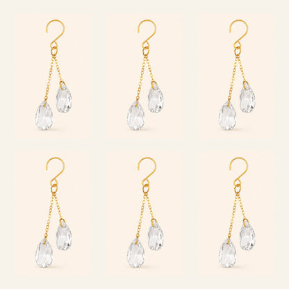 Six clear crystal plant vine suncatcher charms with gold-tone hooks arranged on a warm ivory background.